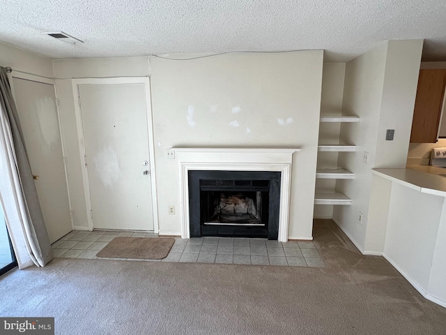 unfurnished living room with a textured ceiling, a fireplace with flush hearth, visible vents, and light colored carpet