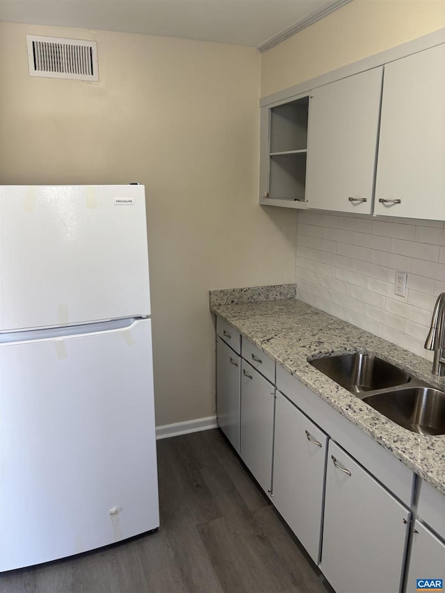 kitchen with light stone counters, a sink, visible vents, white cabinetry, and freestanding refrigerator