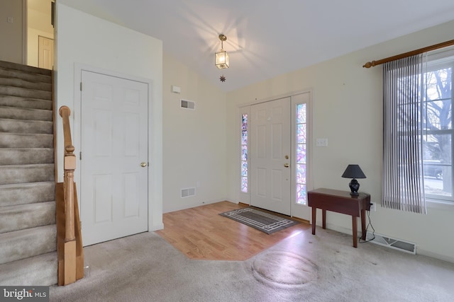 foyer entrance with lofted ceiling, stairway, visible vents, and a healthy amount of sunlight