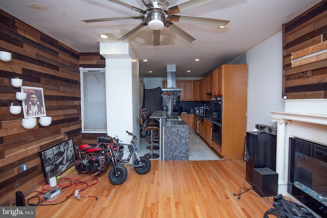 kitchen with wooden walls, island range hood, brown cabinetry, a glass covered fireplace, and light wood-type flooring