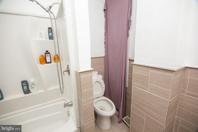 full bath featuring toilet,  shower combination, tile walls, and wainscoting