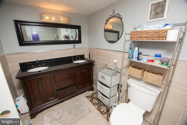 full bath with visible vents, double vanity, a sink, and tile walls