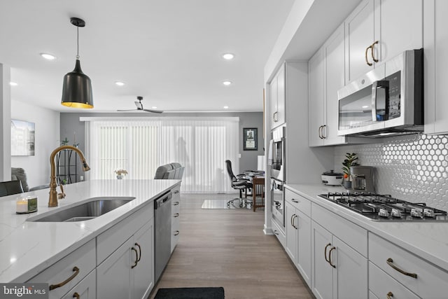 kitchen featuring pendant lighting, stainless steel appliances, a sink, light wood finished floors, and tasteful backsplash