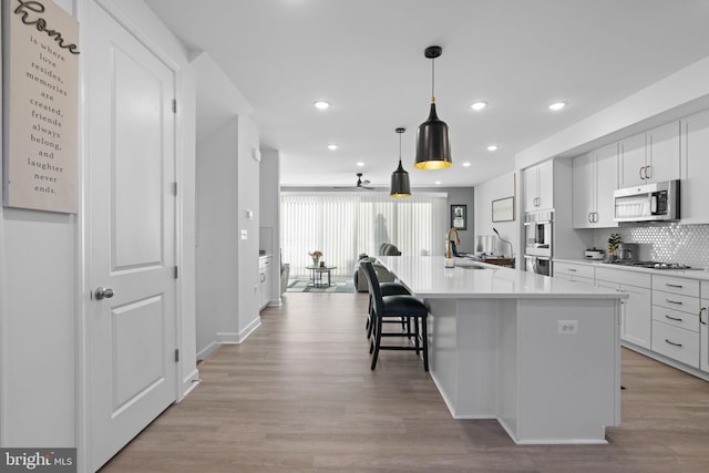 kitchen featuring tasteful backsplash, a kitchen island with sink, stainless steel appliances, light wood-type flooring, and white cabinetry