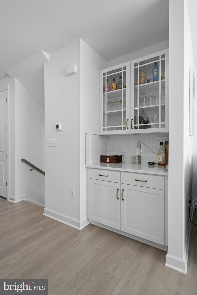 bar featuring backsplash, light wood-style flooring, and baseboards