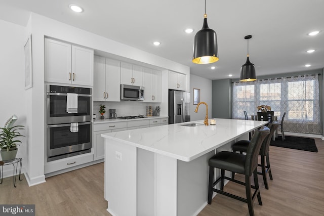 kitchen featuring a kitchen island with sink, a sink, light wood-style floors, appliances with stainless steel finishes, and backsplash