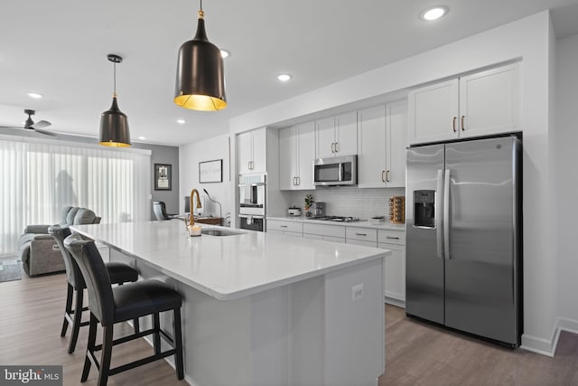 kitchen with wood finished floors, a sink, open floor plan, appliances with stainless steel finishes, and tasteful backsplash