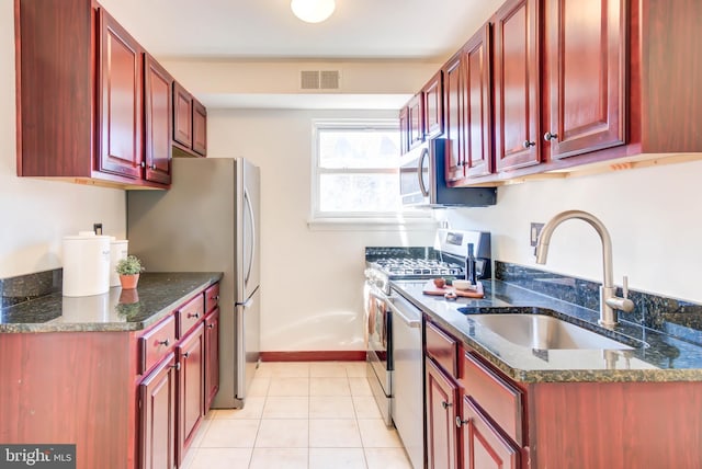 kitchen with dark stone counters, a sink, visible vents, and reddish brown cabinets