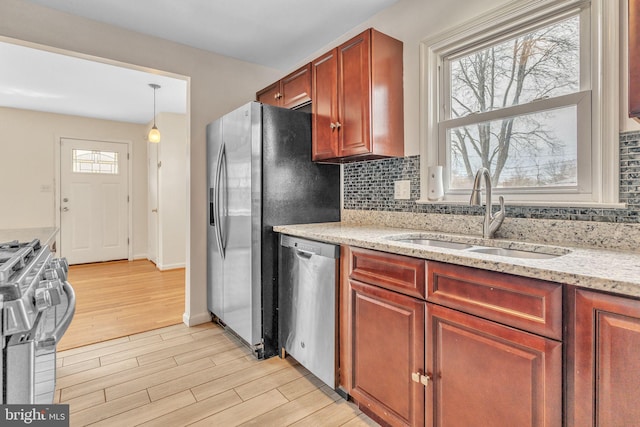 kitchen featuring stainless steel appliances, hanging light fixtures, decorative backsplash, light wood-style floors, and a sink