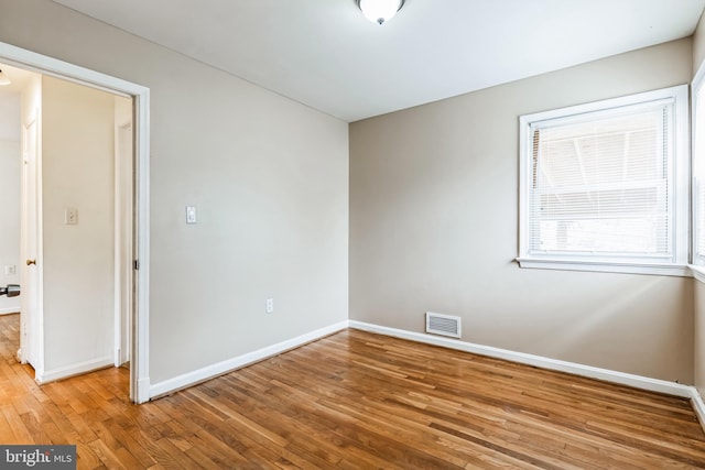 unfurnished room with wood-type flooring, visible vents, and baseboards