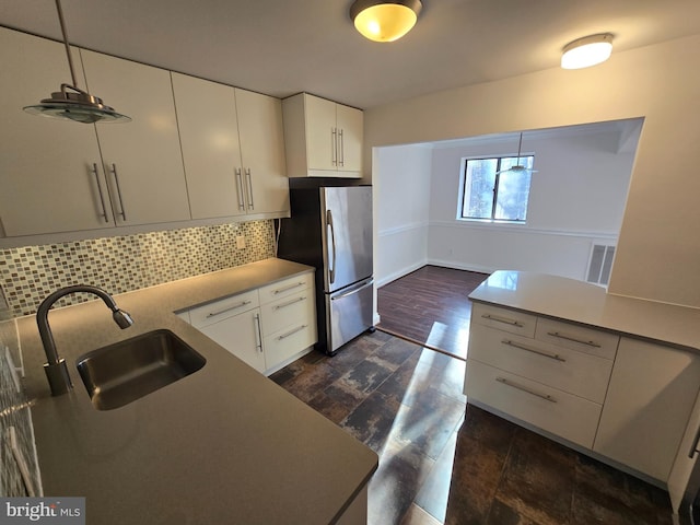 kitchen featuring freestanding refrigerator, white cabinets, a sink, and decorative backsplash