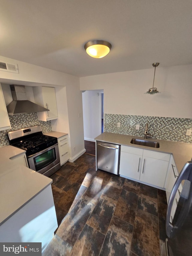 kitchen featuring white cabinets, decorative backsplash, stainless steel appliances, wall chimney range hood, and a sink