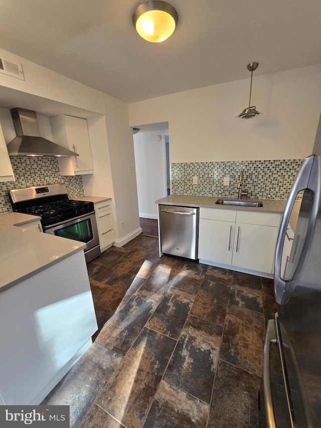 kitchen featuring stainless steel appliances, tasteful backsplash, white cabinetry, a sink, and wall chimney exhaust hood