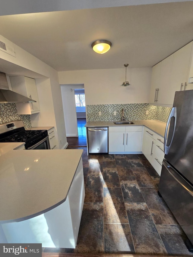 kitchen featuring stainless steel appliances, wall chimney exhaust hood, a sink, and white cabinetry