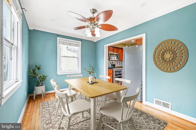 dining room featuring ceiling fan, light wood-style flooring, visible vents, baseboards, and crown molding