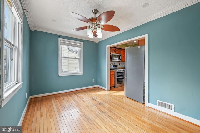 empty room with crown molding, visible vents, light wood-style flooring, ceiling fan, and baseboards