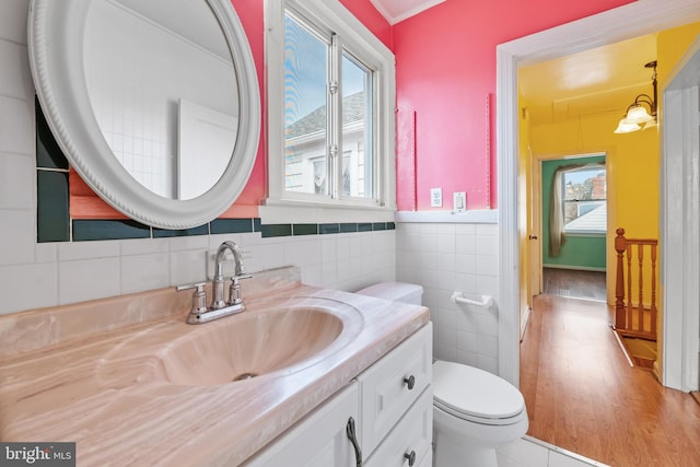 half bathroom with toilet, a wainscoted wall, tile walls, and vanity