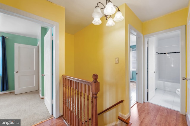 hallway with a chandelier, wood finished floors, an upstairs landing, and baseboards