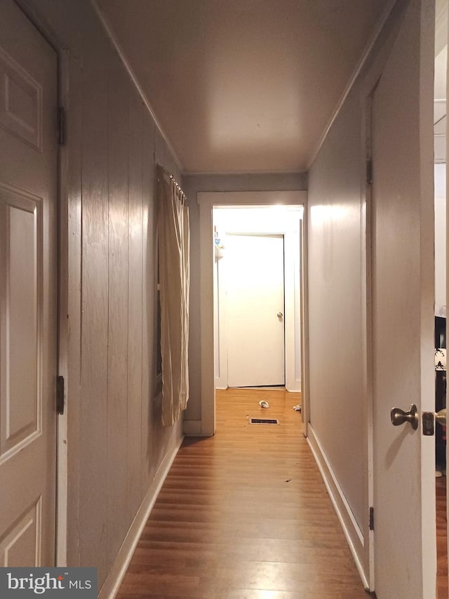 hallway featuring baseboards, wood finished floors, visible vents, and wooden walls