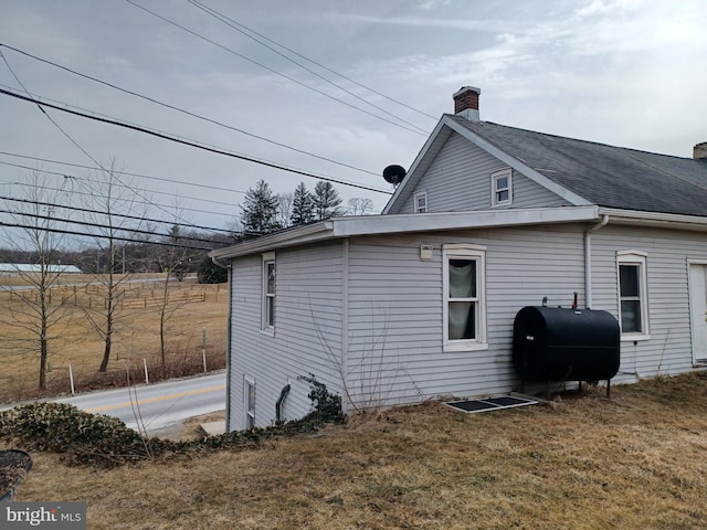 view of side of property with roof with shingles, a lawn, a chimney, and heating fuel