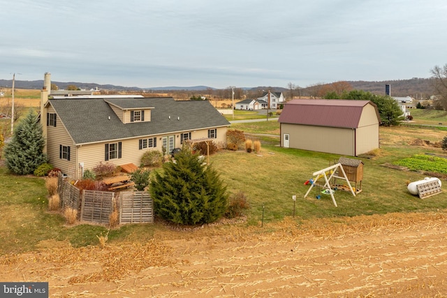 back of property featuring a shingled roof, an outbuilding, an outdoor structure, and a lawn