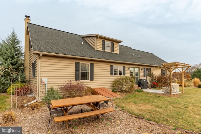 back of house with a pergola, roof with shingles, a lawn, and a patio