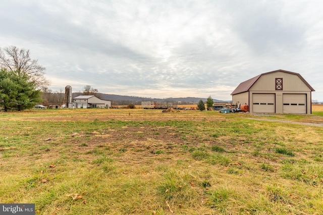 view of yard featuring a garage, a rural view, an outdoor structure, and a barn