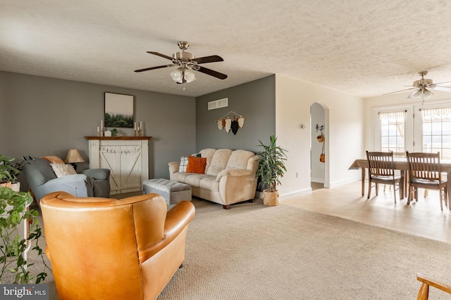 living area with baseboards, visible vents, arched walkways, a ceiling fan, and a textured ceiling