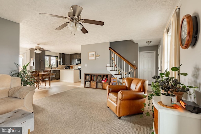 living area with light carpet, ceiling fan, stairway, and a textured ceiling