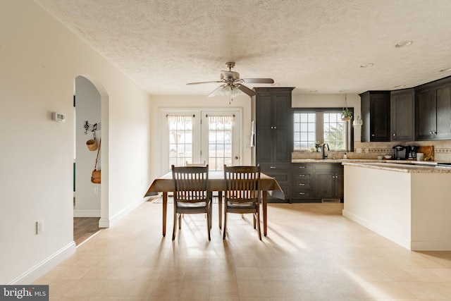 dining room with a ceiling fan, arched walkways, a textured ceiling, and baseboards