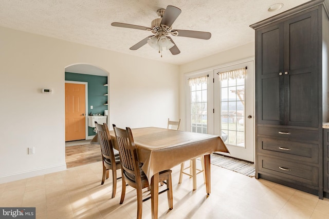 dining area featuring a ceiling fan, arched walkways, a textured ceiling, and baseboards