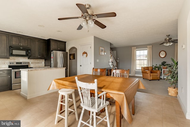 dining room with light tile patterned floors, arched walkways, baseboards, ceiling fan, and stairway