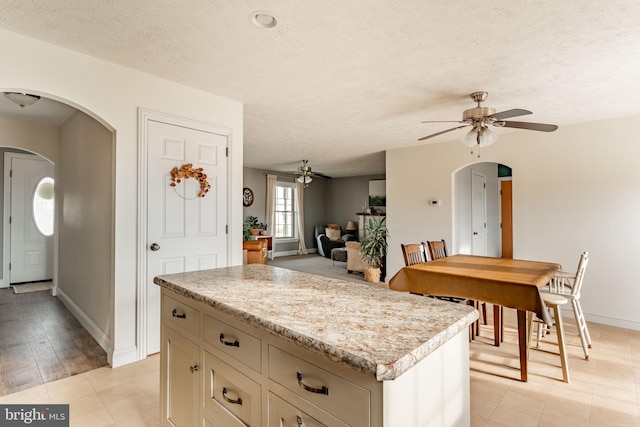 kitchen with arched walkways, ceiling fan, a center island, light countertops, and a textured ceiling