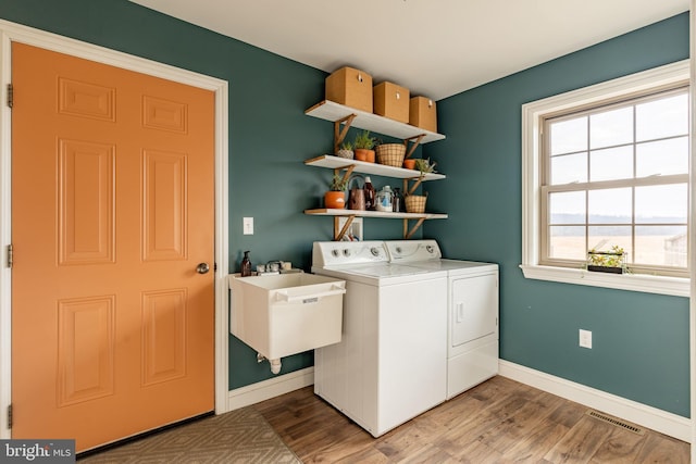 laundry room featuring washer and clothes dryer, visible vents, a sink, wood finished floors, and laundry area