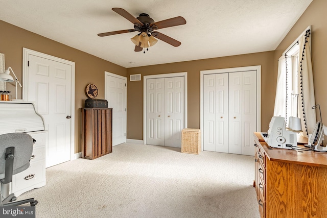 interior space featuring multiple closets, visible vents, ceiling fan, a textured ceiling, and baseboards