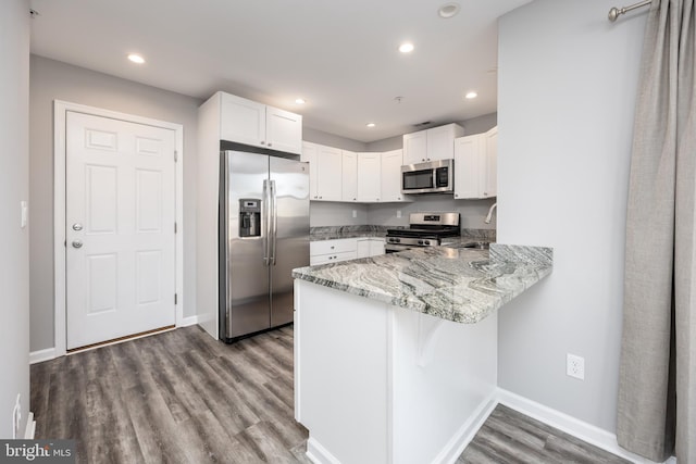 kitchen featuring light stone countertops, wood finished floors, a peninsula, appliances with stainless steel finishes, and white cabinetry