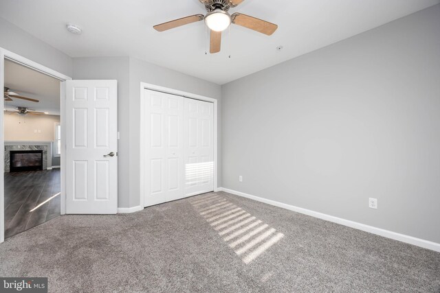 unfurnished bedroom featuring carpet, baseboards, a fireplace, ceiling fan, and a closet