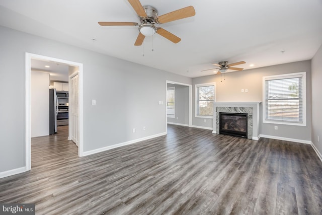 unfurnished living room featuring a healthy amount of sunlight, dark wood-type flooring, baseboards, and ceiling fan