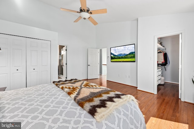 bedroom with a closet, a towering ceiling, a ceiling fan, wood finished floors, and baseboards