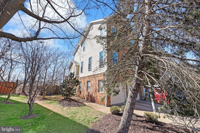 view of home's exterior with brick siding, a lawn, an attached garage, and fence