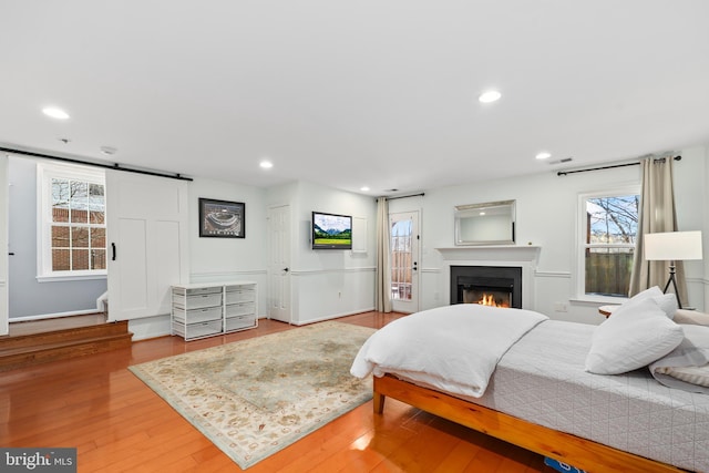 bedroom featuring recessed lighting, a barn door, wood finished floors, a warm lit fireplace, and baseboards