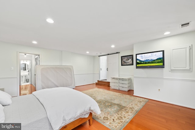 bedroom featuring a barn door, visible vents, wood finished floors, and recessed lighting