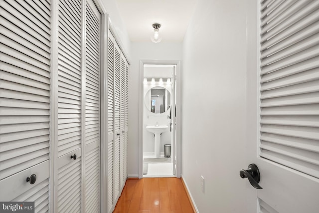 corridor featuring light wood-style floors, baseboards, and a sink