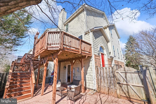 back of property featuring a patio, a chimney, a gate, a wooden deck, and stairs