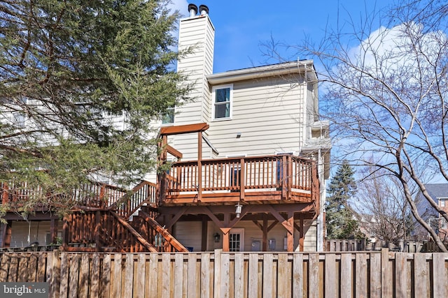 rear view of house with a fenced front yard, a chimney, a wooden deck, and stairs