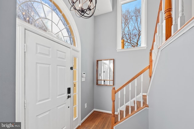 entryway featuring baseboards, wood finished floors, an inviting chandelier, a high ceiling, and stairs