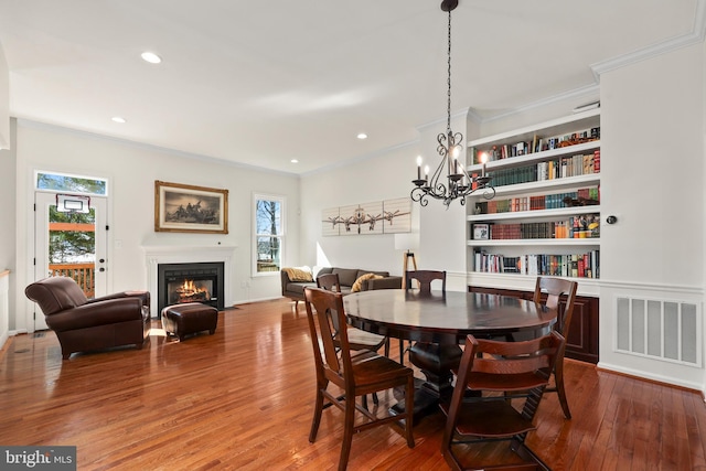 dining area with a fireplace with flush hearth, visible vents, wood finished floors, and ornamental molding