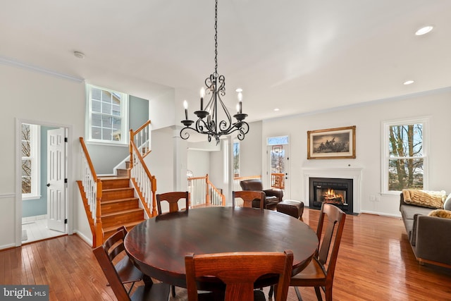 dining area with light wood finished floors, recessed lighting, a glass covered fireplace, baseboards, and stairs