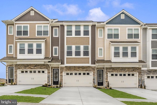 townhome / multi-family property with a garage, stone siding, and concrete driveway