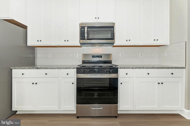 kitchen featuring stone counters, light wood-style flooring, appliances with stainless steel finishes, and white cabinets